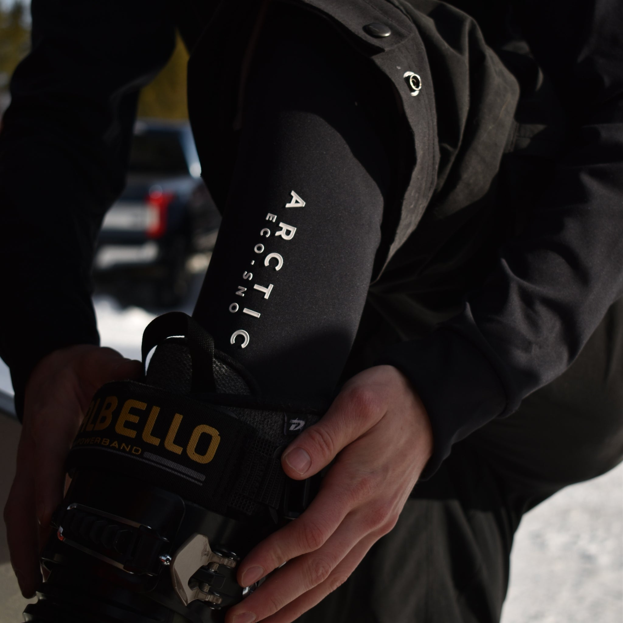 Close-up of black Arctic Eco-Sno thermal base layer sleeve worn while fastening ski boot, designed for cold weather layering.