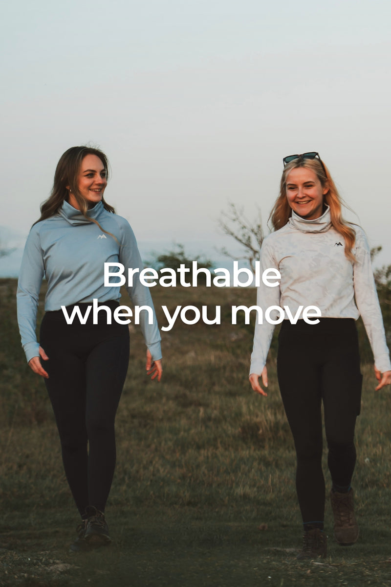 Two women walking outdoors in base layers, one in a light blue long-sleeve top and black leggings, and the other in a white long-sleeve top and black leggings. Large white text across the center reads 'Breathable when you move'.