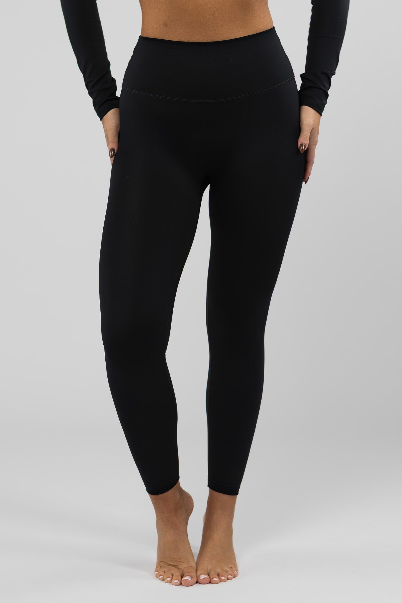 Woman wearing high-waisted black thermal leggings, standing with feet slightly apart in a studio setting.