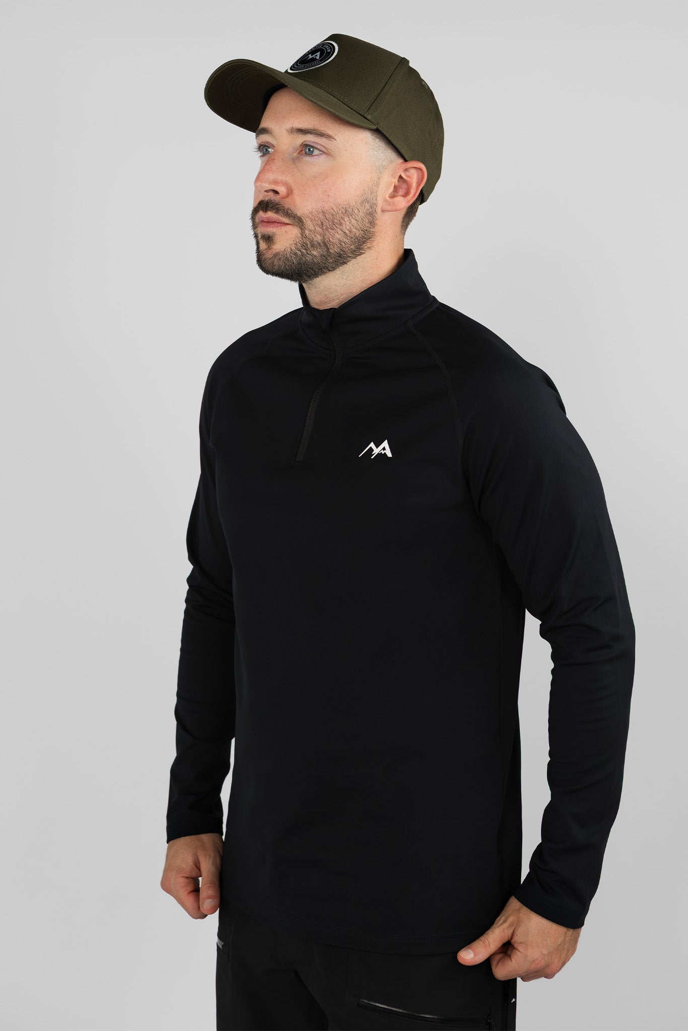 Man wearing a black thermal quarter-zip base layer, standing in a neutral pose and looking to the side in a studio setting.