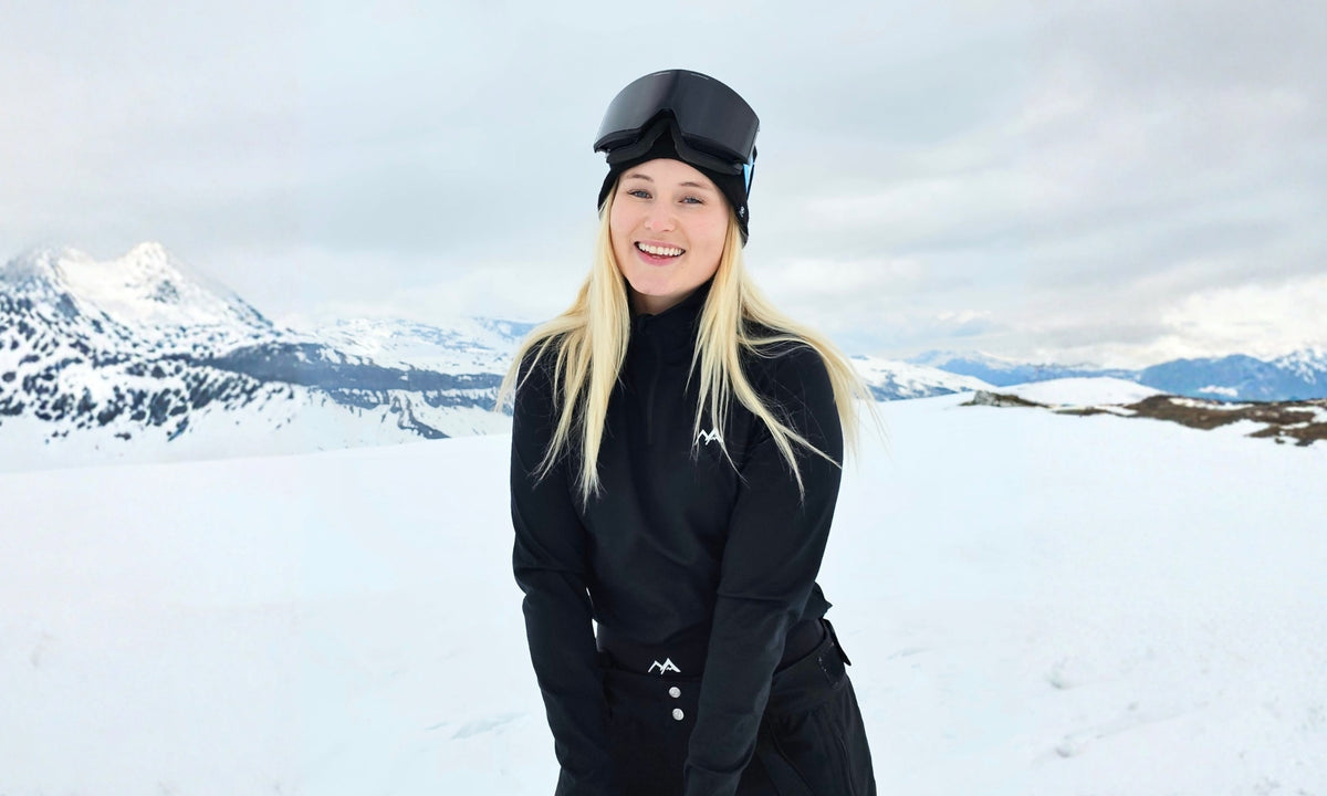 woman in black arctic eco sno base layer set with goggles on a snowy mountain background