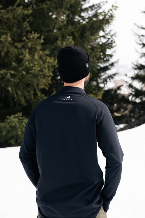 Back view of Man wearing mens black base layer top standing in the snow with trees in background