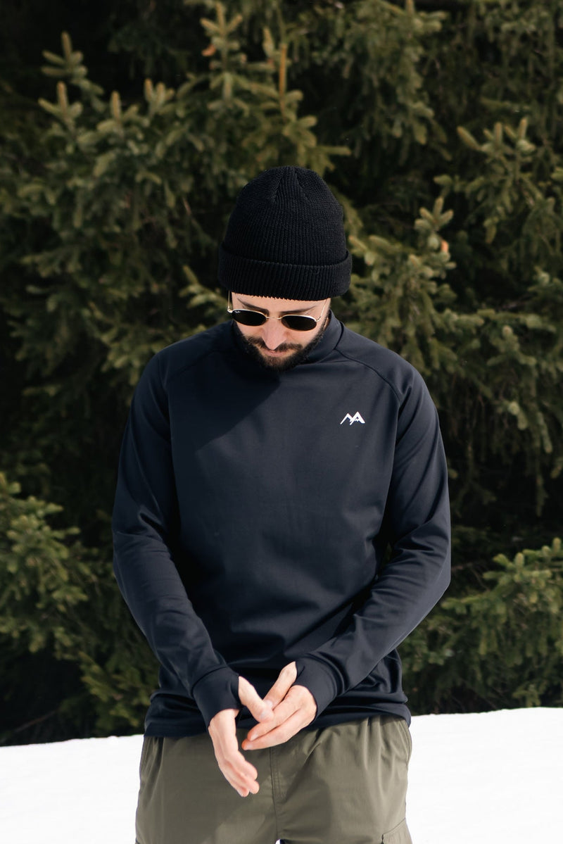 Man wearing mens black base layer top standing in the snow with trees in background