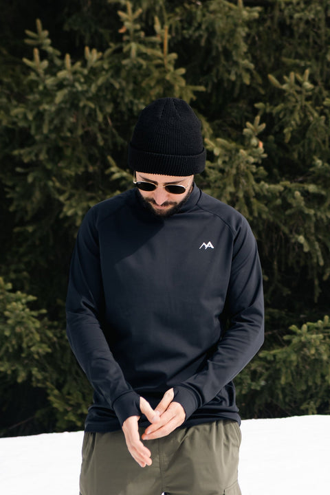 Man wearing mens black base layer top standing in the snow with trees in background